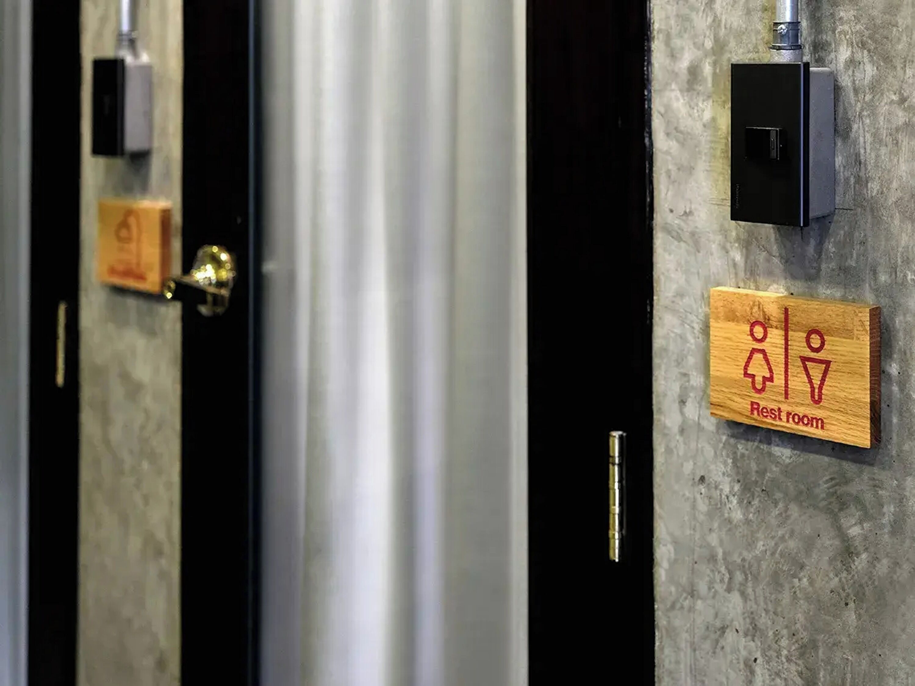 Des toilettes avec une pancarte en bois indiquant « toilettes », une poignée de porte en métal et une boîte électrique fixée au mur.