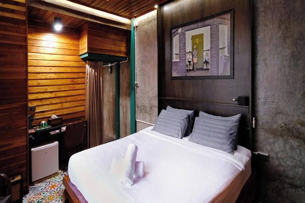 Ein Hotelzimmer mit Holzbalkendecke, einem Bett mit weißen Leinentüchern, einem Nachttisch, einem kleinen Tisch und einem Wandbild.