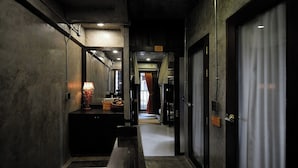 Um corredor estreito com um banco, um espelho, um abajur e uma porta que dá para um quarto.