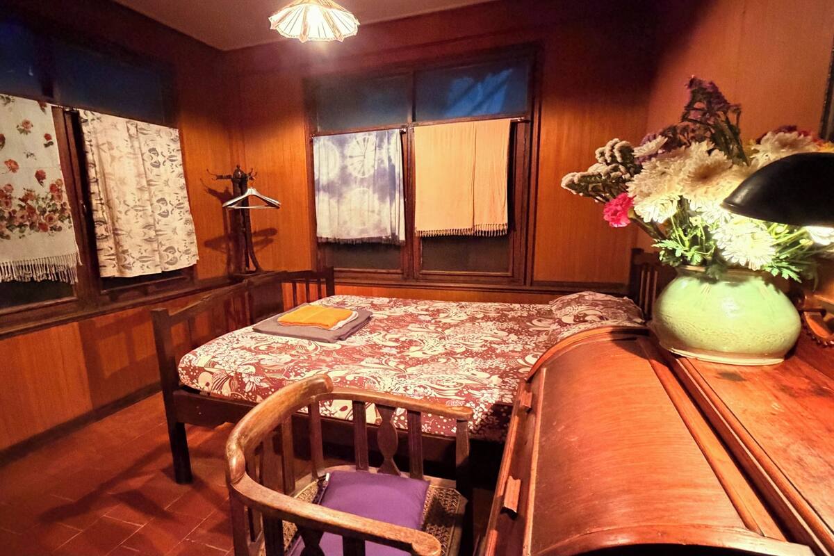 Une pièce comprenant une table en bois, une chaise, un banc, un luminaire suspendu et une fenêtre avec des rideaux.