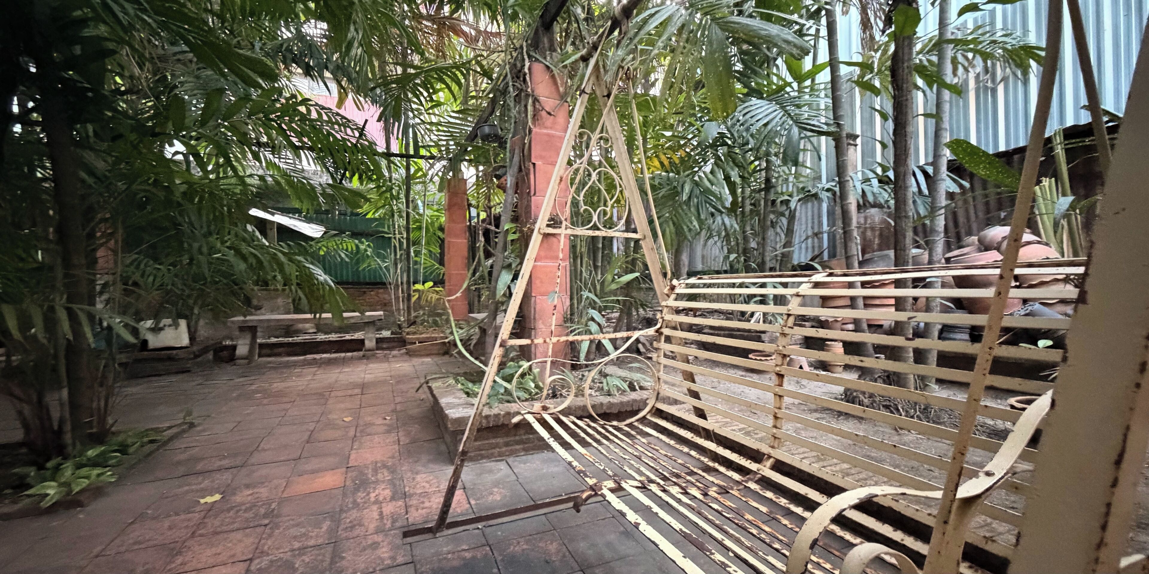 A courtyard with a metal bench, potted plants, and a brick wall.