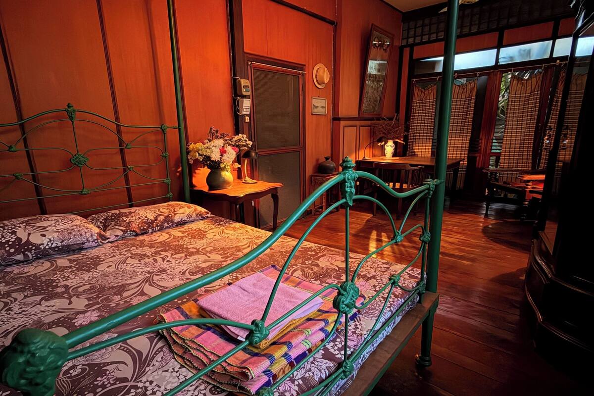 Une pièce comprenant un lit, une petite table avec un vase de fleurs, un miroir et une fenêtre avec des rideaux.