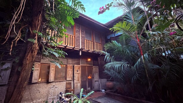 Un bâtiment en bois doté d’un balcon, entouré d’une végétation tropicale luxuriante.