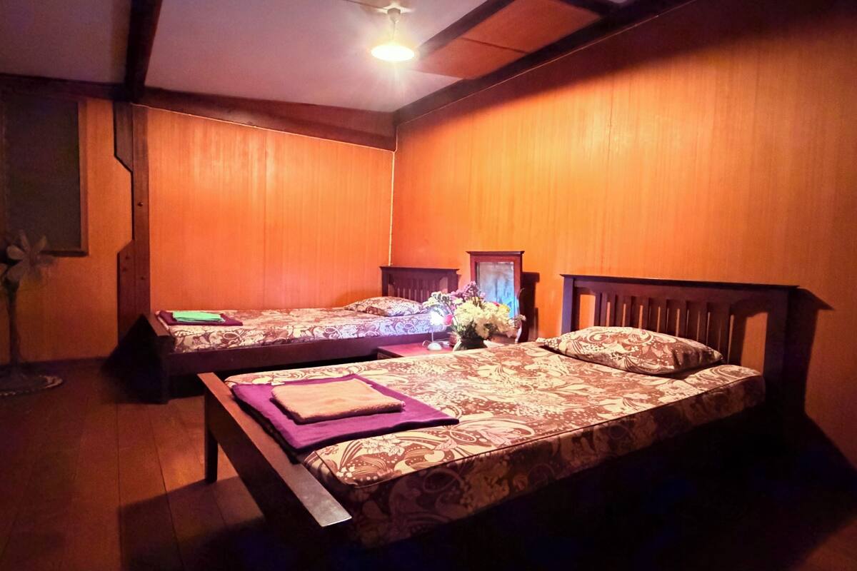 Une chambre avec deux lits, des murs en bois et un ventilateur de plafond.