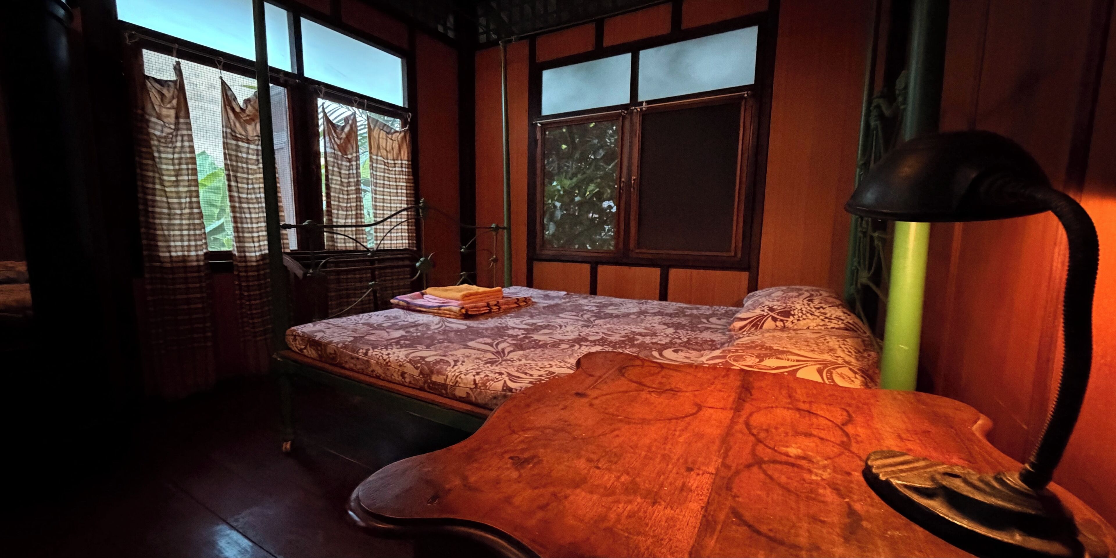 A room with a bed, a desk, a lamp, and a window with curtains.