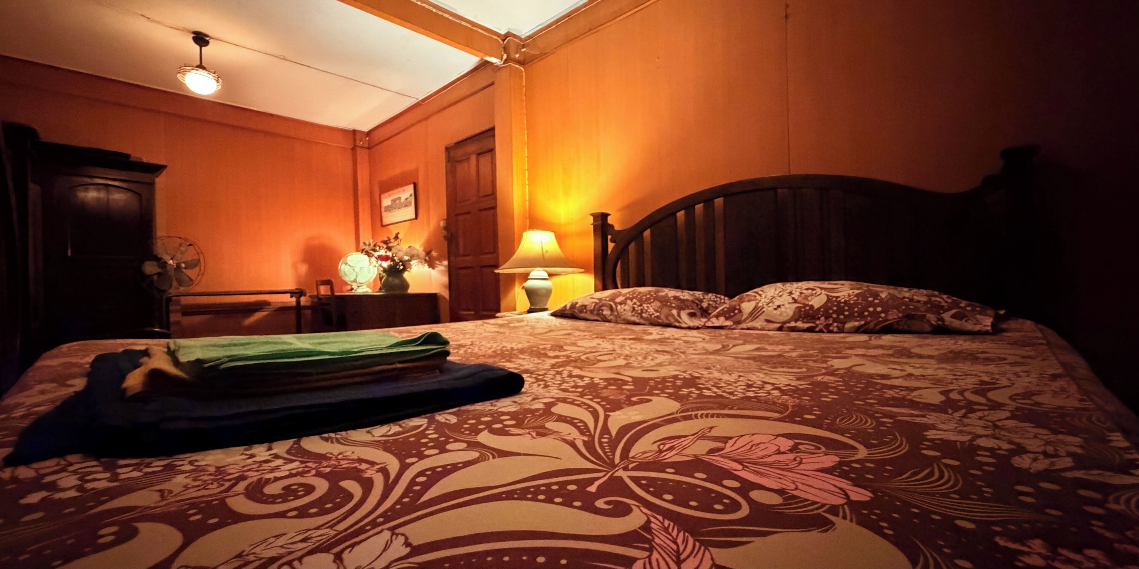 A bedroom with a bed, a dresser, a lamp, and a fan.