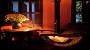 Une pièce avec une table ronde, une chaise en osier, un vase rempli de fleurs et une fenêtre donnant sur des arbres.