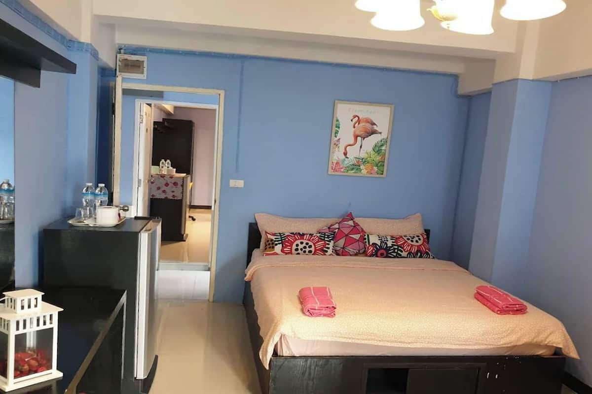 A hotel room with a bed, a desk with a lamp, a small table with a lantern, and a door leading to a bathroom.