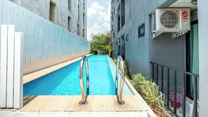 A narrow swimming pool with metal railings, surrounded by buildings with balconies and an air conditioning unit on the right. - Chill Guest (Bangkok)