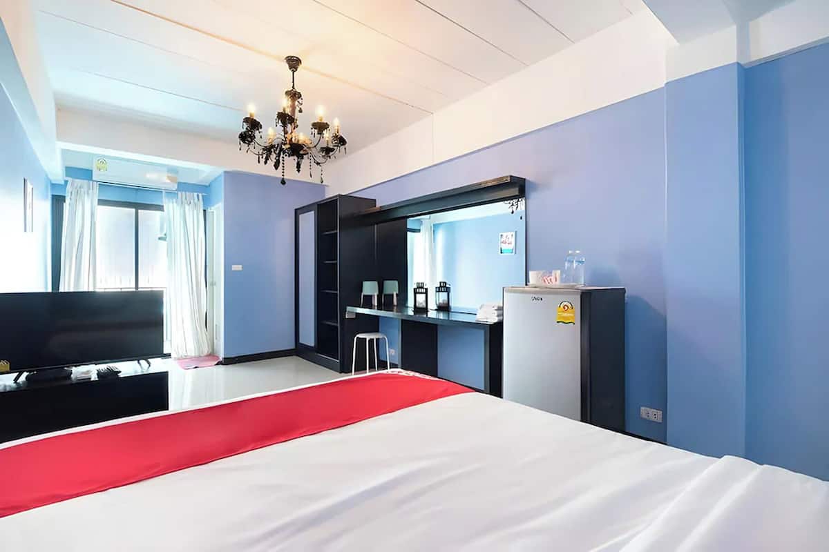 A hotel room with a bed, a TV, a desk, a refrigerator, and a chandelier.
