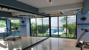 A gym with exercise equipment, large windows, and a view of a swimming pool. - Chill Guest (Bangkok)