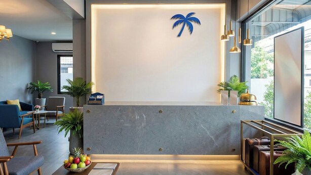 A reception area with a modern design, featuring a reception desk, seating area, and potted plants. - Chill Guest (Bangkok)