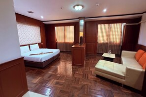 Ein Hotelzimmer mit Bett, einer Couch, einem kleinen Tisch, einem Spiegel und einem Fenster mit Vorhängen.
