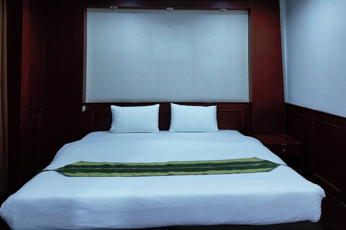 Une chambre d’hôtel avec un grand lit, une tête de lit, une table de chevet et une fenêtre avec un store.