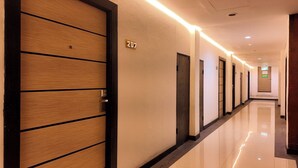 Un couloir d’hôtel avec des portes en bois, un panneau indiquant le numéro des chambres, et un sol propre et brillant.