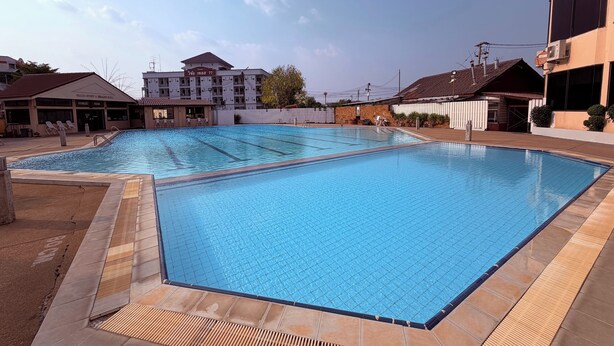 A swimming pool with tiled edges, adjacent buildings, and a fenced area. - G2 Ayutthaya (Uthai)