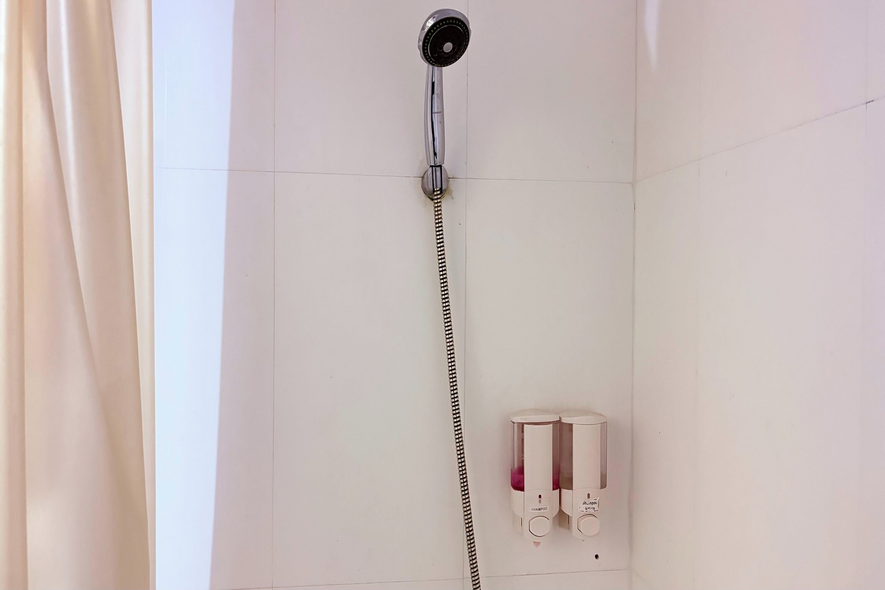 A shower with a handheld hose, a control panel, and two shampoo bottles.