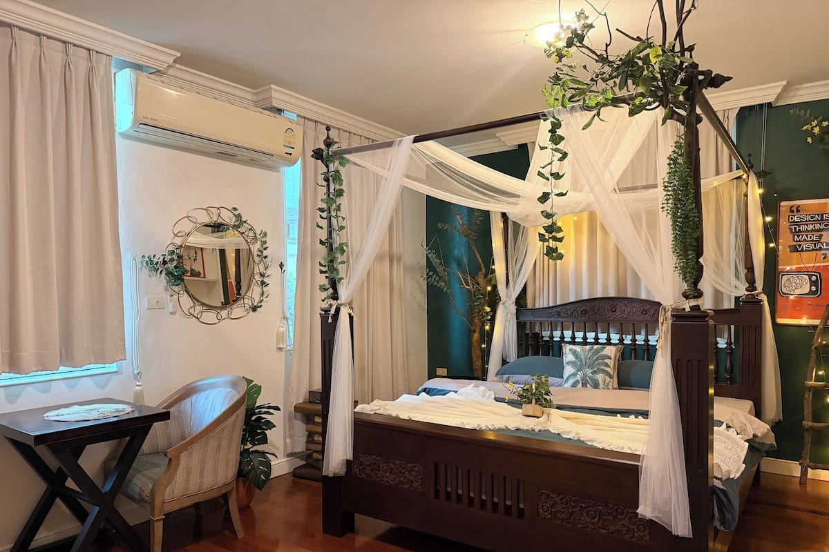 Una cama con dosel y cuatro columnas, un escritorio con silla, un espejo y una planta colgante en la pared.