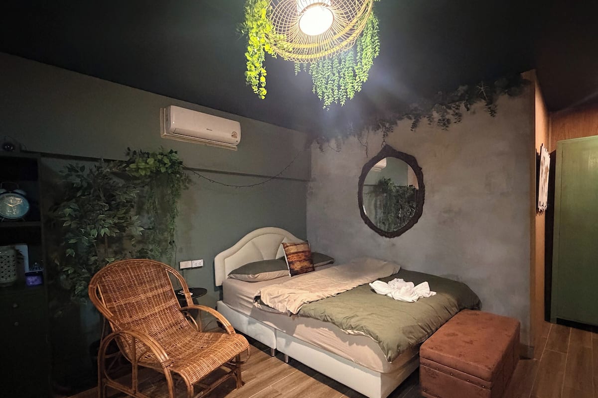 Un dormitorio con una cama, una silla, una mesita, aire acondicionado y un espejo en la pared.