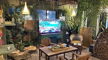 A cozy indoor setting with a television, wooden furniture, and lush greenery.