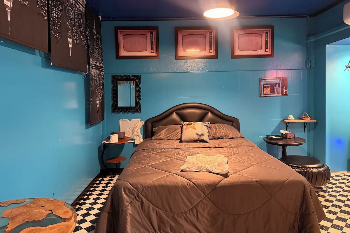 Una habitación con una cama, una mesa redonda, un espejo y tres televisores enmarcados en la pared.