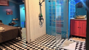 Une pièce avec un sol à carreaux, un lit, une douche avec une porte en verre, un lavabo avec un pare-éclaboussures bleu et un néon.