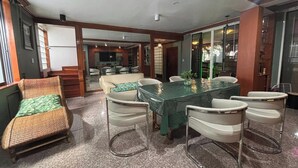 Un coin repas avec une table à plateau en verre, des chaises blanches et un canapé en osier.