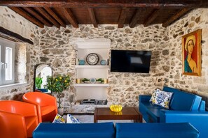 A stone-walled living room with a TV, orange and blue furniture, a wooden ceiling, and a painting. - Art House Seaview & Jacuzzi Spartylas Sleeps 4 (corfu)