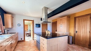 A kitchen with wooden cabinets, a central island, a stainless steel range hood, and a dining area visible through an open doorway. - Little Balloch Angus Glens (Kirriemuir)