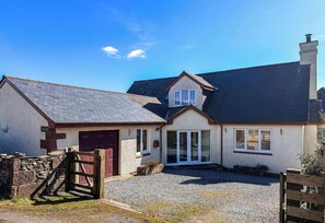 A two-story house with a gravel driveway, a red door, and a chimney. - Little Balloch Angus Glens (Kirriemuir)