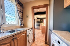A kitchen with a washing machine, a sink, and a window with curtains. - Little Balloch Angus Glens (Kirriemuir)