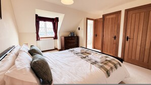 A bedroom with a bed, a dresser, a window with curtains, and wooden doors. - Little Balloch Angus Glens (Kirriemuir)