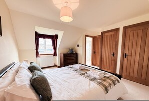 A bedroom with a bed, a dresser, a window with curtains, and wooden doors. - Little Balloch Angus Glens (Kirriemuir)