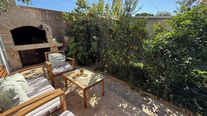 Patio esterno con camino in pietra, mobili in legno e vegetazione rigogliosa.