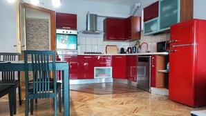 Una cucina compatta con mobili rossi, un tavolo da pranzo in legno e un tappeto blu.