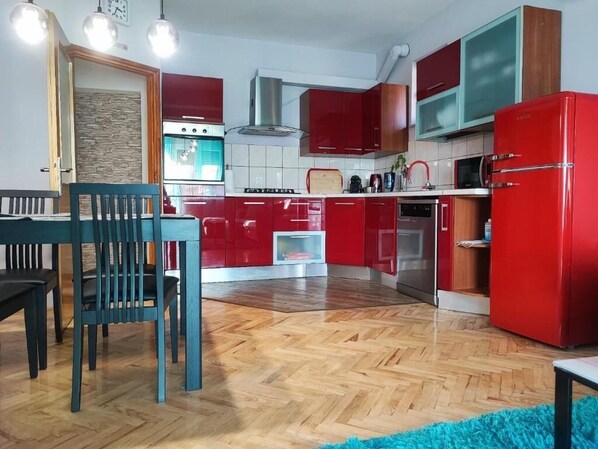 Eine kleine Küche mit roten Schränken, einem Holztisch und einem blauen Teppich.