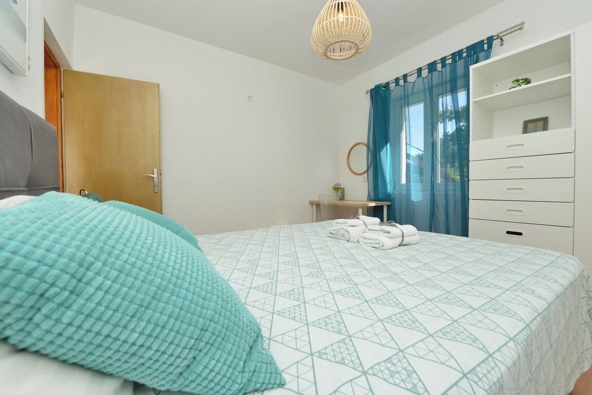 A bedroom with a bed, a bedside table, a mirror, a wardrobe, and a hanging light fixture.