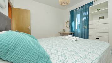 A bedroom with a bed, a bedside table, a mirror, a wardrobe, and a hanging light fixture.