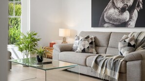En moderne stue med en grå sofa, mønstrede puder, et glasbord, en lampe og et stort billede i ramme på væggen.