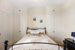 Un dormitorio con una cama, paredes blancas, dos puertas y una mesita de noche con lámpara.