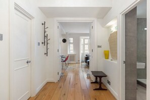 A hallway with wooden flooring, white walls, a coat rack, a clock, and a window with a view. - GuestReady - Chic London Retreat with Balcony (London)