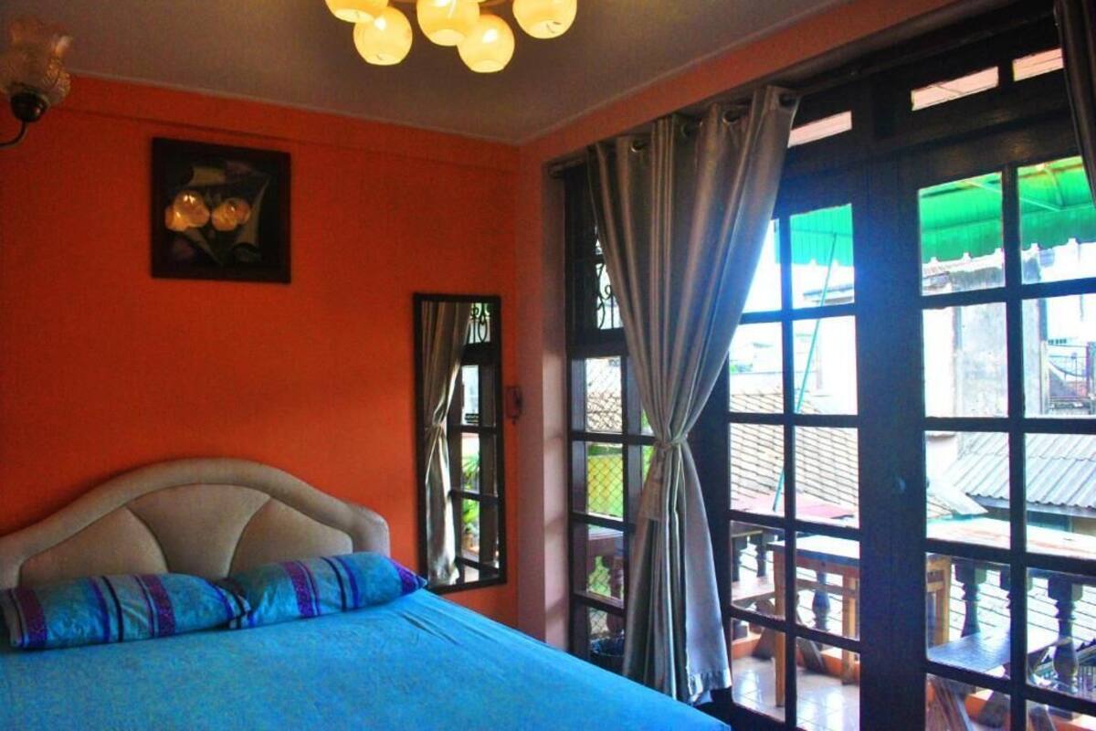 Ein Schlafzimmer mit Bett, Fenster mit Vorhängen und Blick ins Freie.