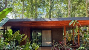 A modern house with a wooden deck, surrounded by lush greenery and tall trees. - Kaia Bungalow – Adults Only Private Pool (Manzanillo)