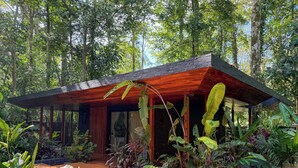 A modern house with a wooden deck, surrounded by lush tropical plants and a small pond. - Kaia Bungalow – Adults Only Private Pool (Manzanillo)