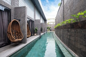 Una piscina interior estrecha con sillas de mimbre y plantas en macetas.