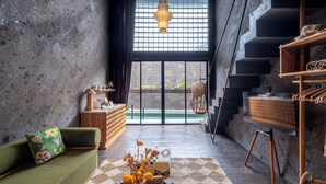 A modern interior with a green sofa, a wooden cabinet, a hanging light fixture, and a staircase. - The Lima Ocean Suites Pererenan (Canggu)