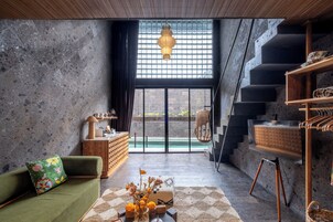 Un interior moderno con un sofá verde, un armario de madera, un colgante de luz y una escalera.