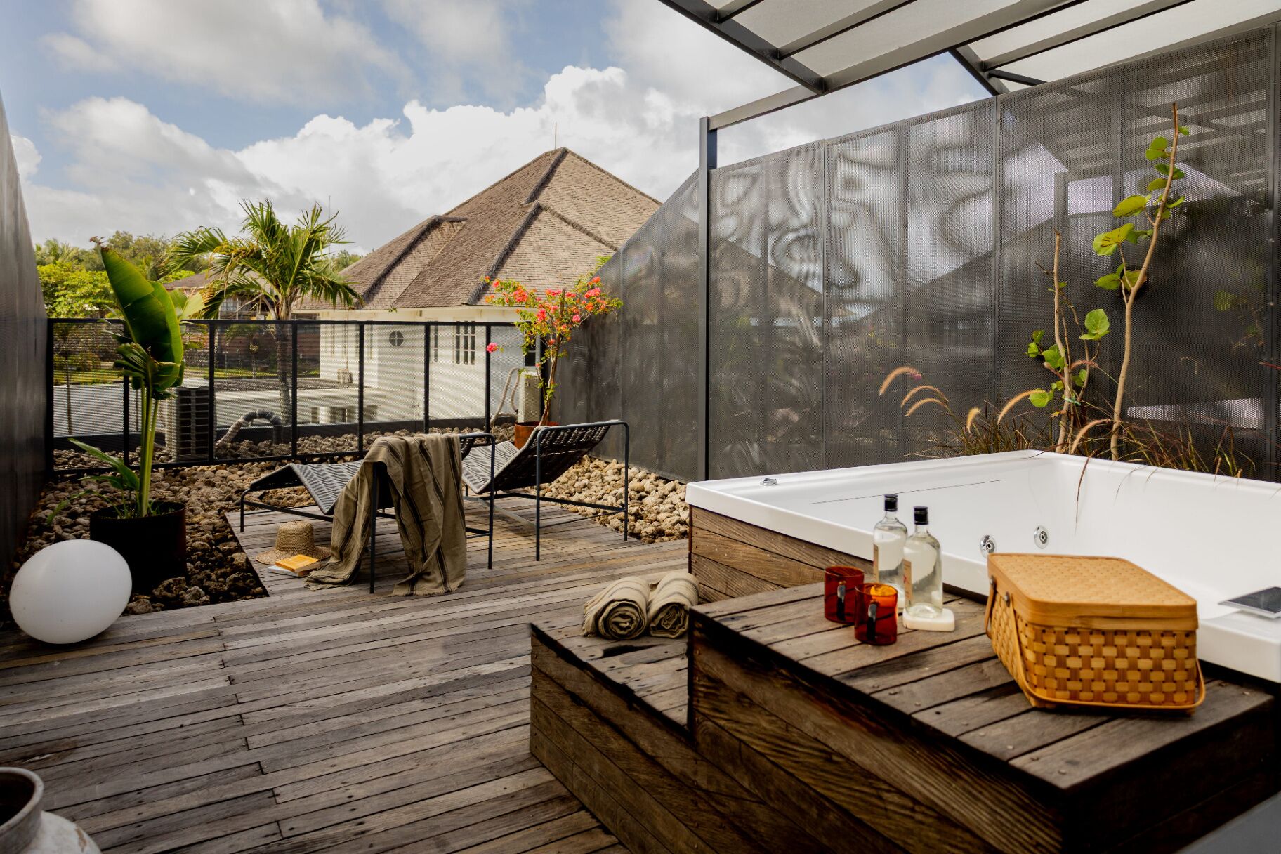 A modern outdoor spa area with a wooden deck, a hot tub, and a view of a building with a pyramid roof.