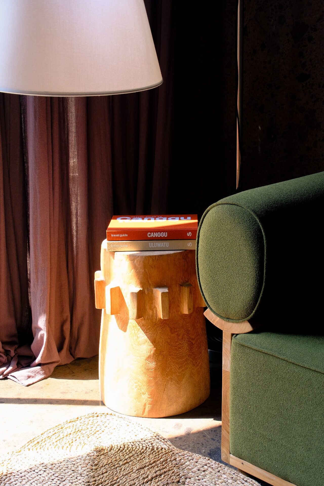 A room with a green armchair, a wooden stool with travel guides, and a lamp.
