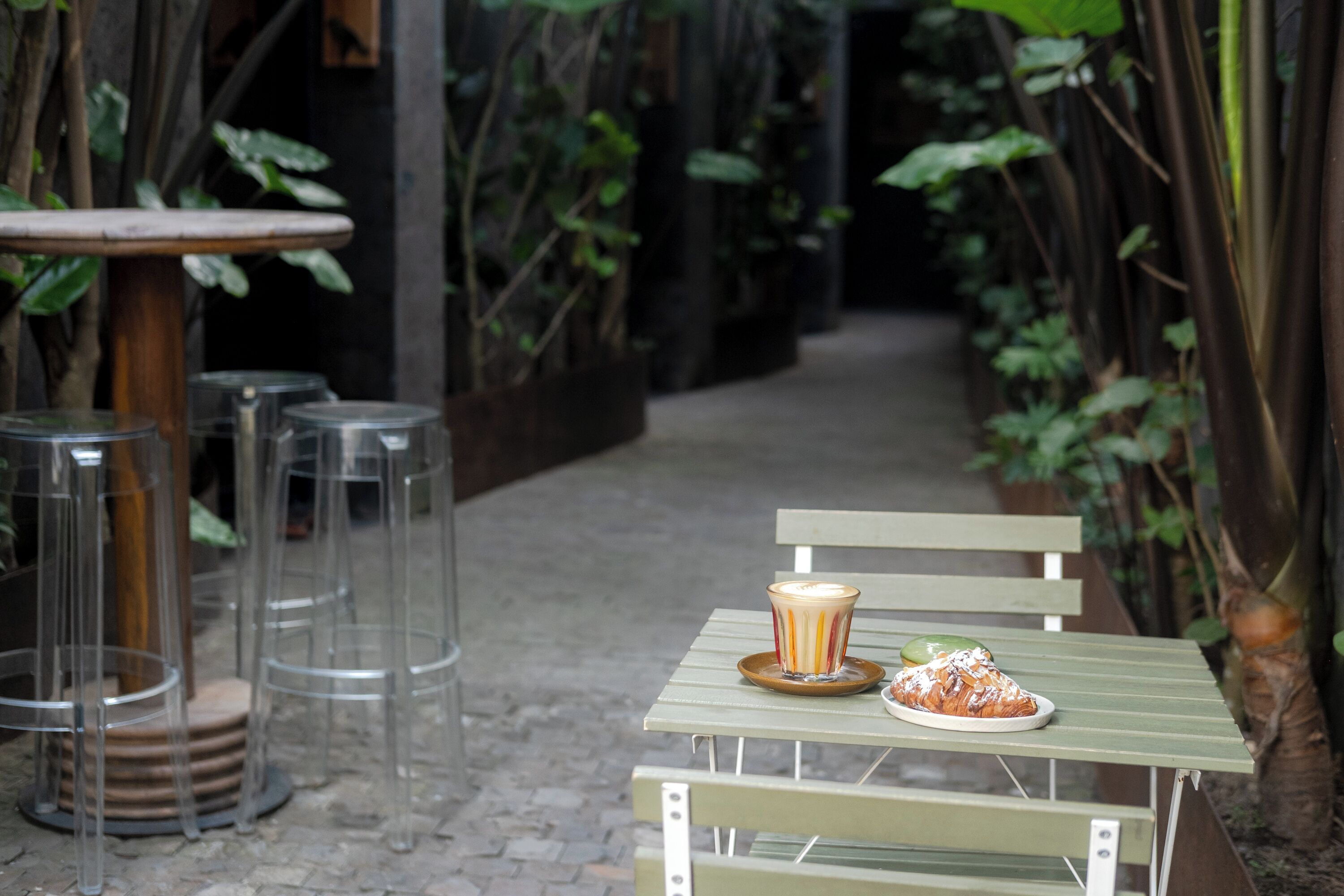 A table with a plate of food and a drink, surrounded by chairs and plants.